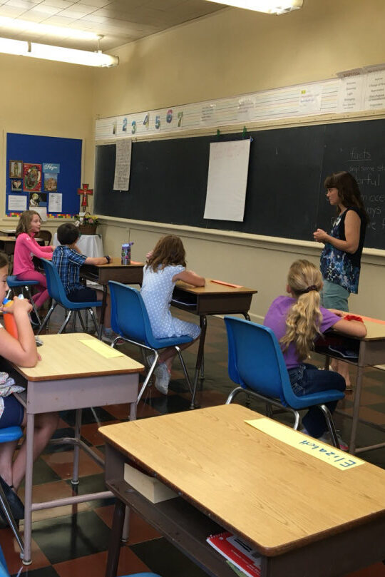 An adult leader teaches a class of elementary students about geology